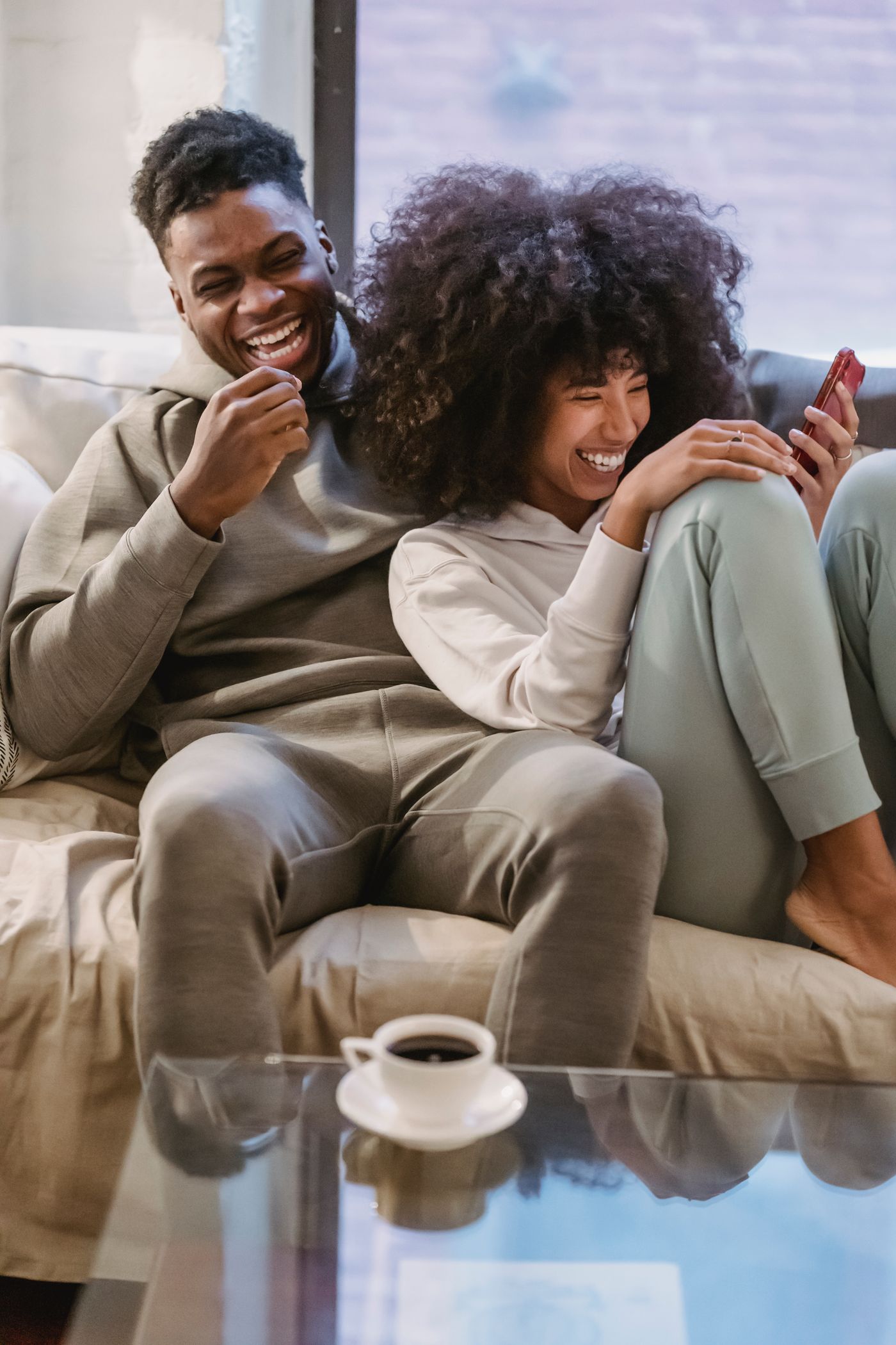 A couple laughing together on a sofa while sharing photos on a phone